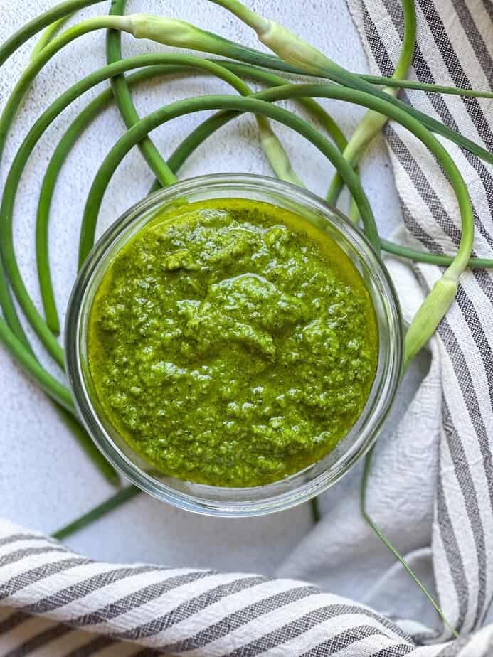 Garlic scape pesto in a bowl with fresh garlic scapes around the bowl.