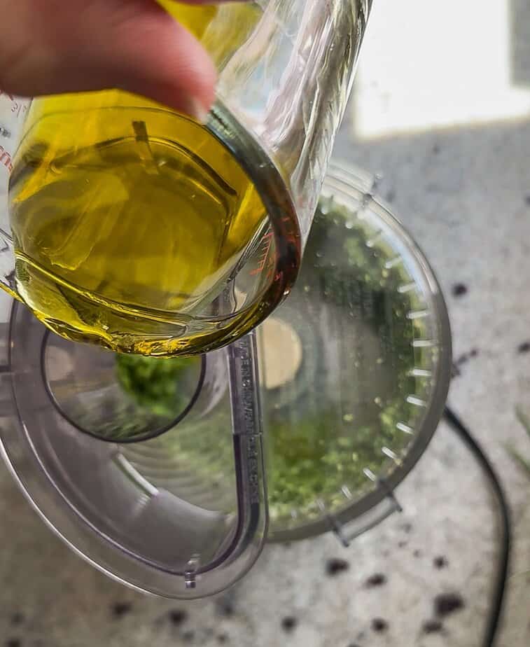 Olive oil pouring into shoot of food processor.