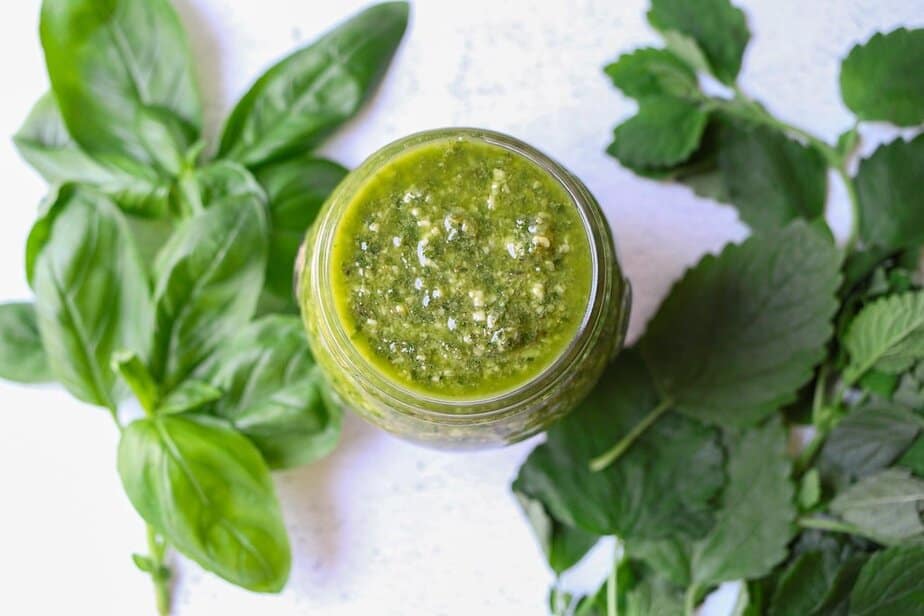 Lemon Balm Pesto in a jar with fresh basil and lemon balm leaves surrounding the jar.