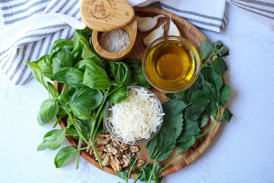 Ingredients for lemon balm pesto: fresh basil and lemon balm leaves, salt, garlic cloves, olive oil, shredded parmesan and walnuts.