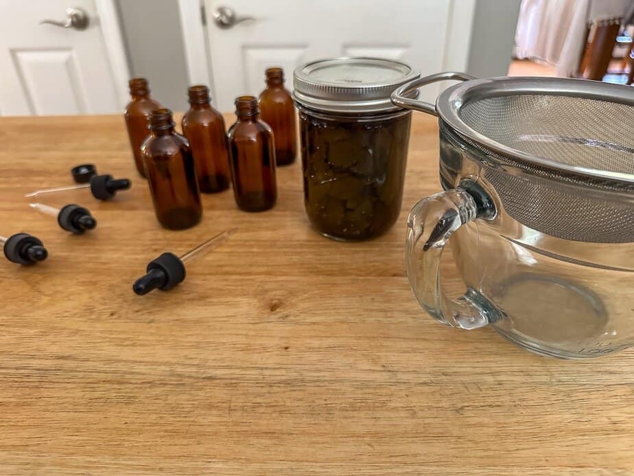 Lemon balm extract that has infused with small jars and strainer on surface.