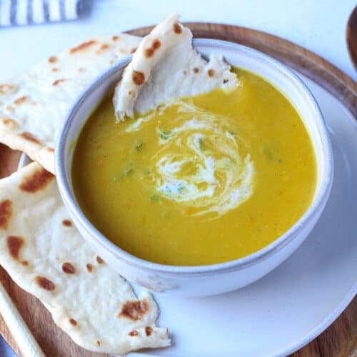 Curried pumpkin apple soup in a white bowl served with naan bread.