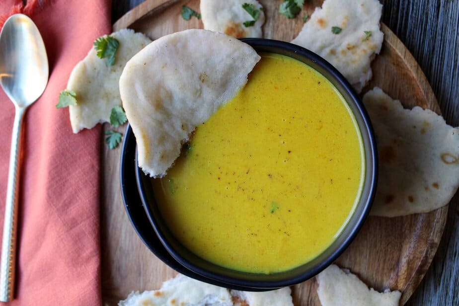 Curried pumpkin apple soup in a dark bowl served with naan bread.