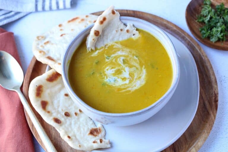 Curried pumpkin apple soup in a white bowl served with naan bread.
