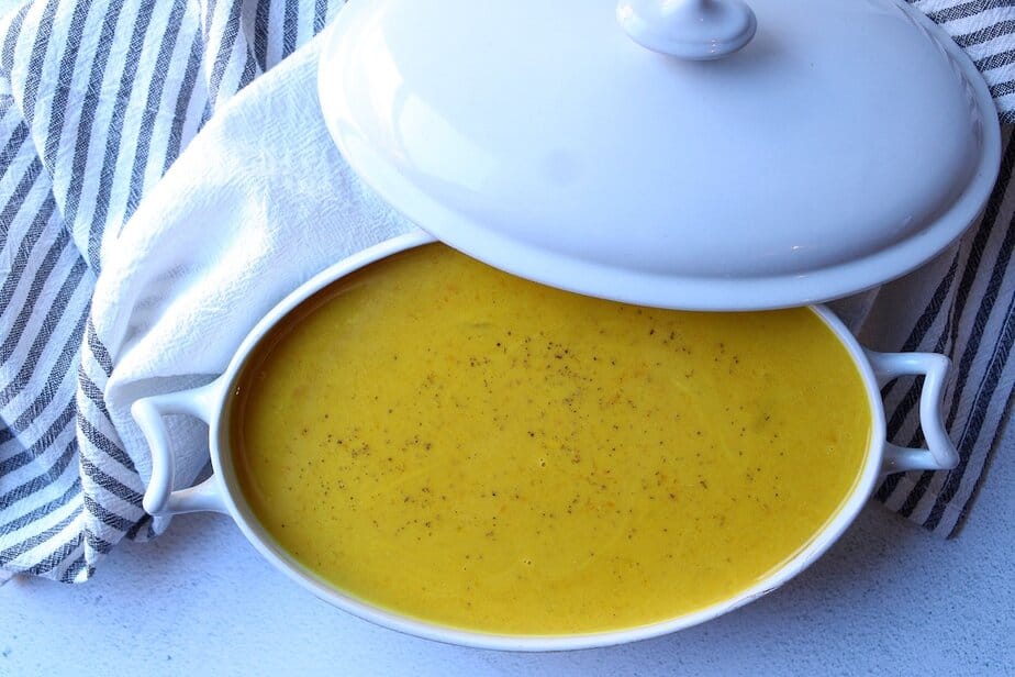 Curried pumpkin apple soup in a white serving bowl with lid.