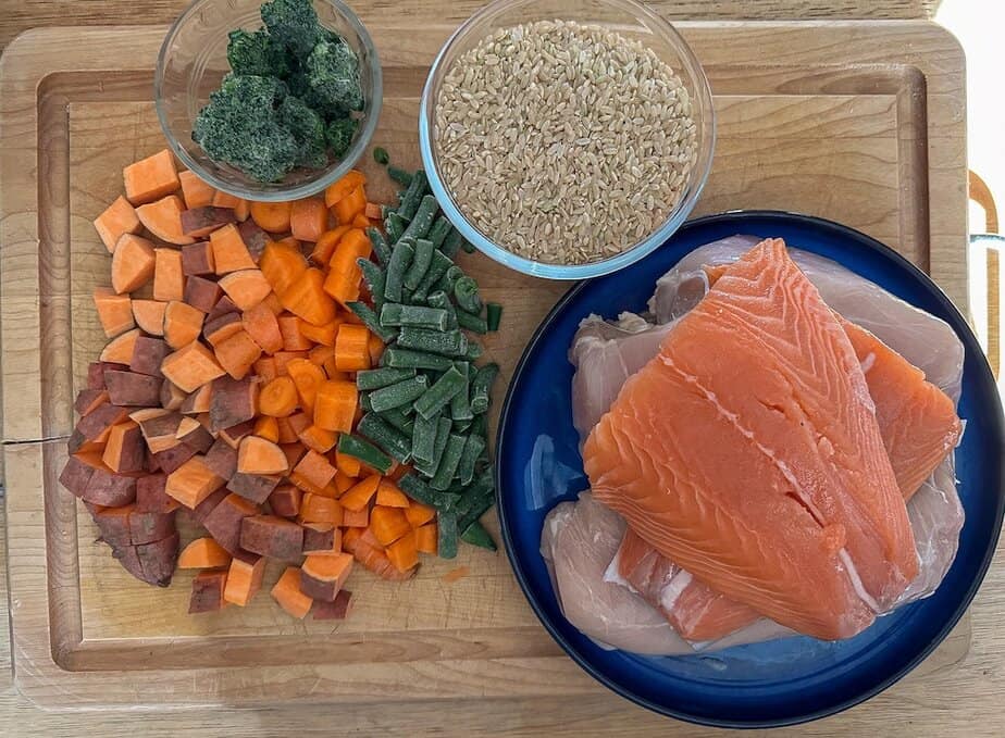Ingredients for homemade salmon and chicken dog food on a wooden board.