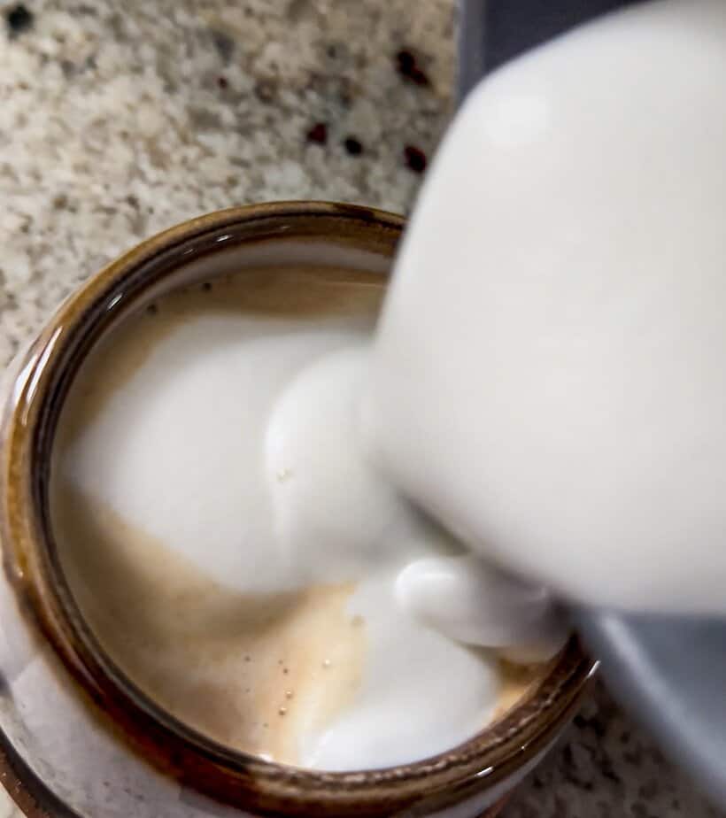 Foam pouring over chai latte in a cup.