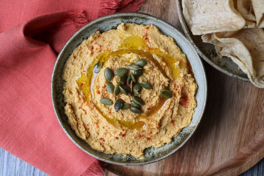 Pumpkin hummus in a bowl with pumpkin seeds, oil and seasoning sprinkled on top.