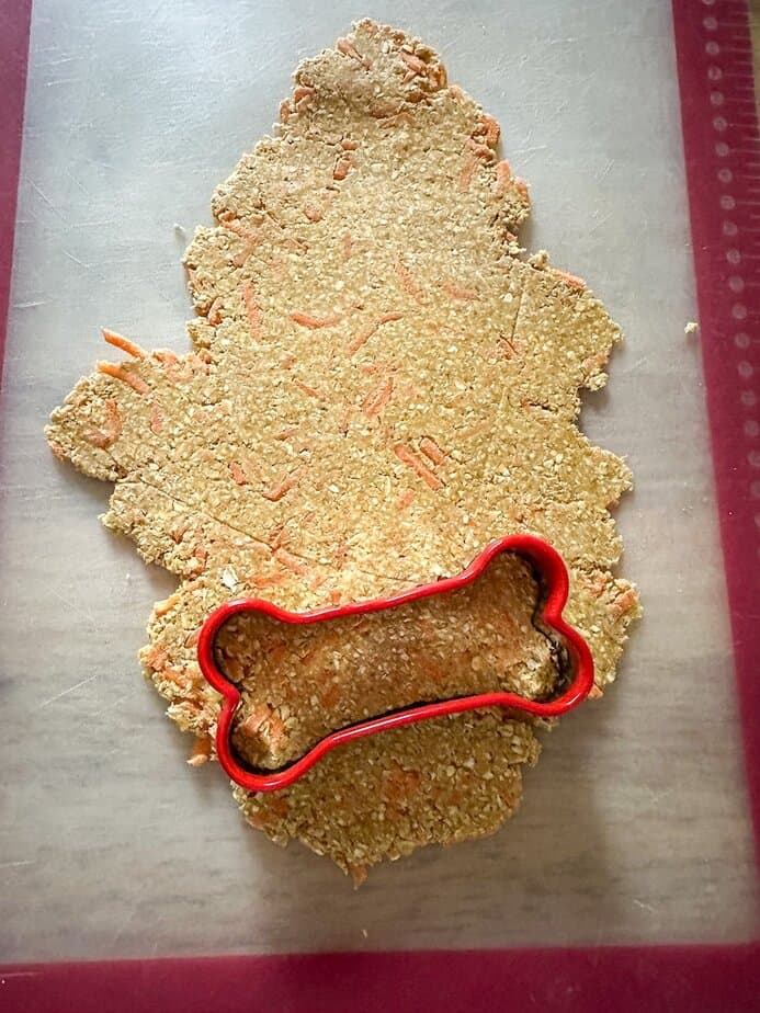Carrot treat dough rolled out on surface with dog-bone shaped cookie cutter.