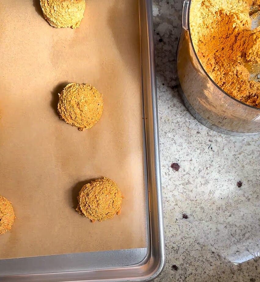 Carrot treat dough scooped onto parchment paper lined baking sheet.