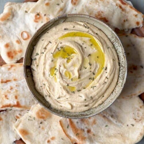 Roasted garlic hummus in a bowl with olive oil and dried herbs drizzled on top.