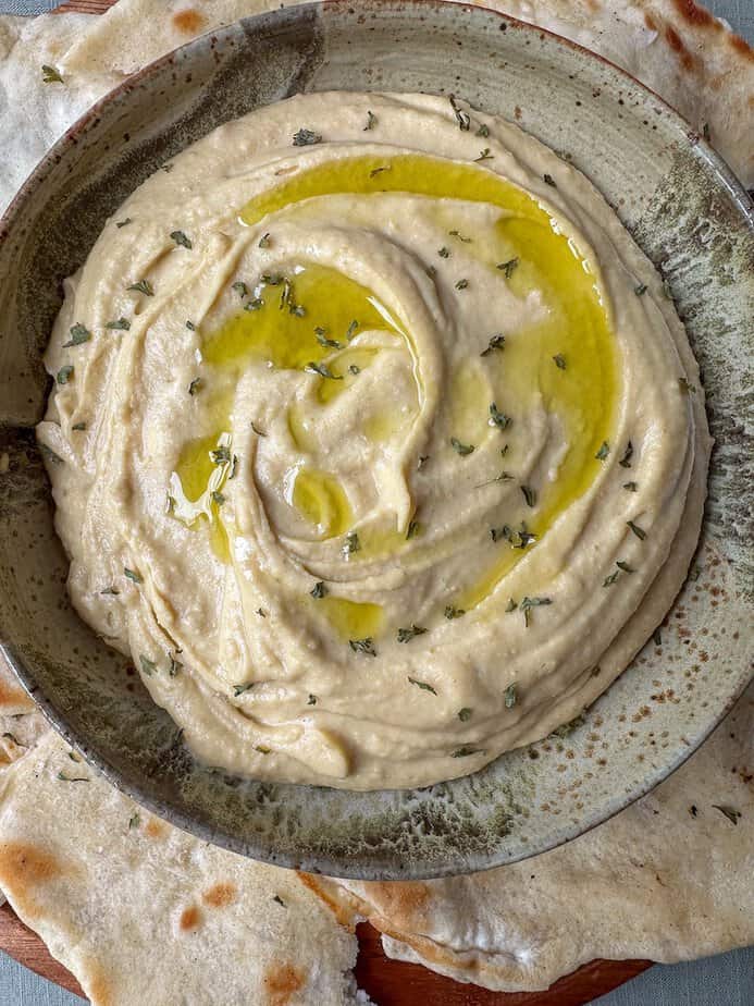 Roasted garlic hummus in a bowl with olive oil and dried herbs drizzled on top.