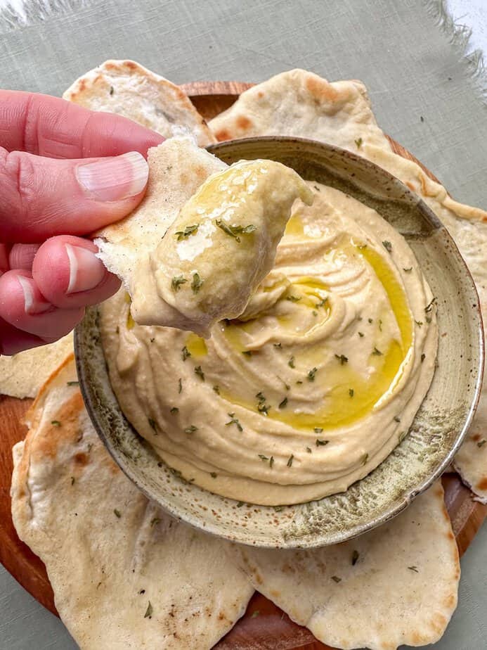 Hand scooping hummus from a bowl.