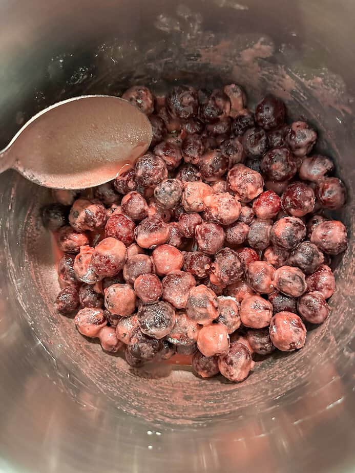 Cornstarch and sugar mixed with frozen cherries in a pot.