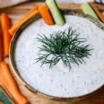 Creamy fresh dill dip in a bowl with carrot and cucumber sticks.