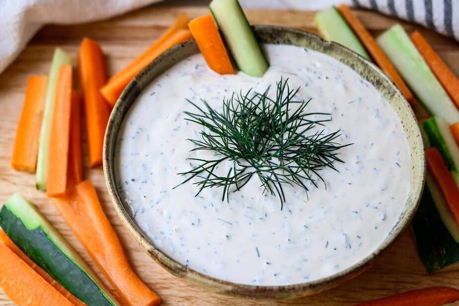 Creamy fresh dill dip in a bowl with carrot and cucumber sticks.