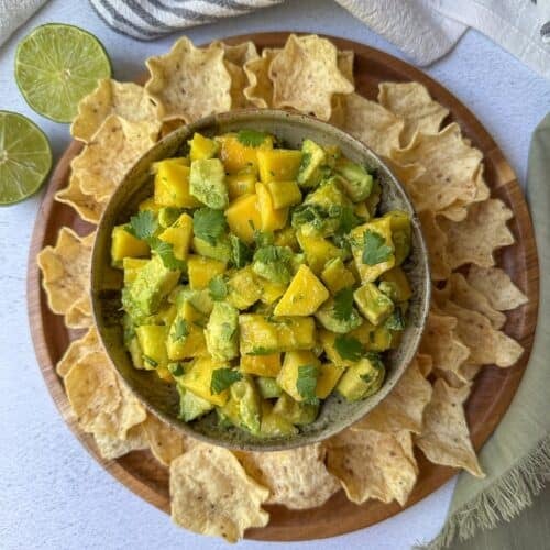Avocado mango salsa in a bowl with tortilla chips around the bowl.