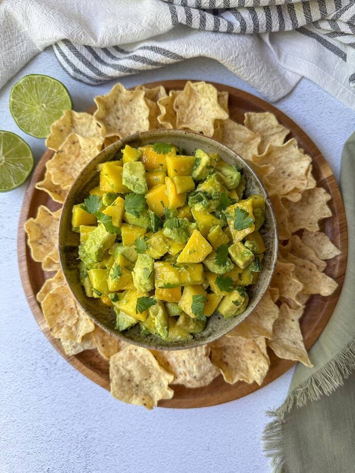 Avocado mango salsa in a bowl with tortilla chips around the bowl.