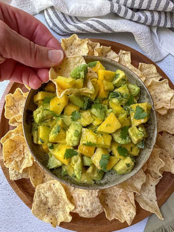Hand scooping avocado mango salsa with a tortilla chip.