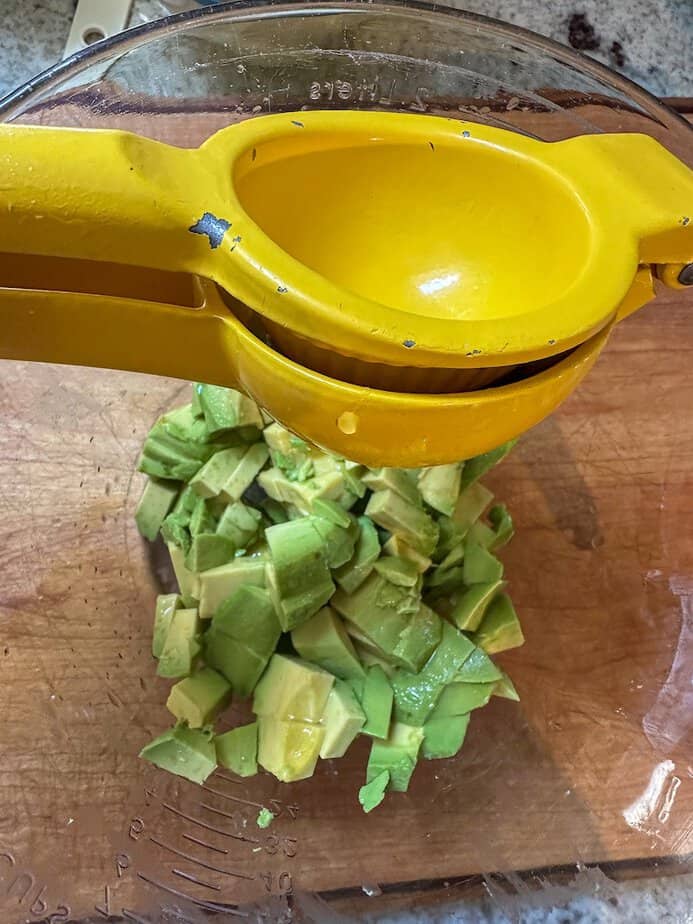 A hand-held juicer squeezing lime juice over chopped avocado.
