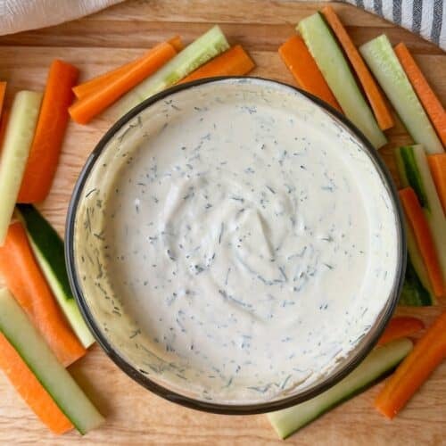 Fresh dill dip in a bowl with fresh vegetables around bowl.