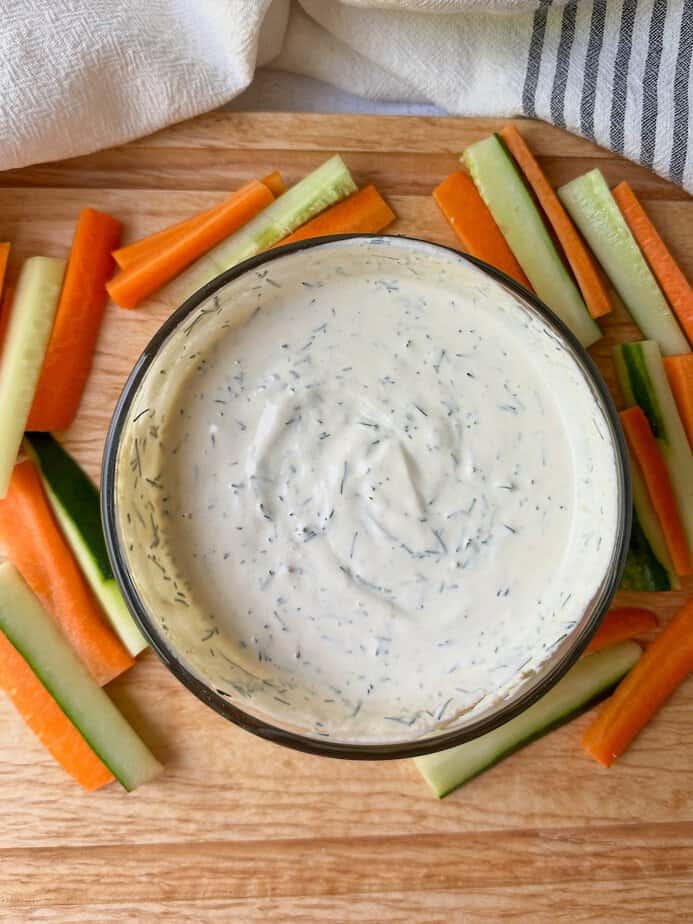 Fresh dill dip in a bowl with fresh vegetables around bowl.