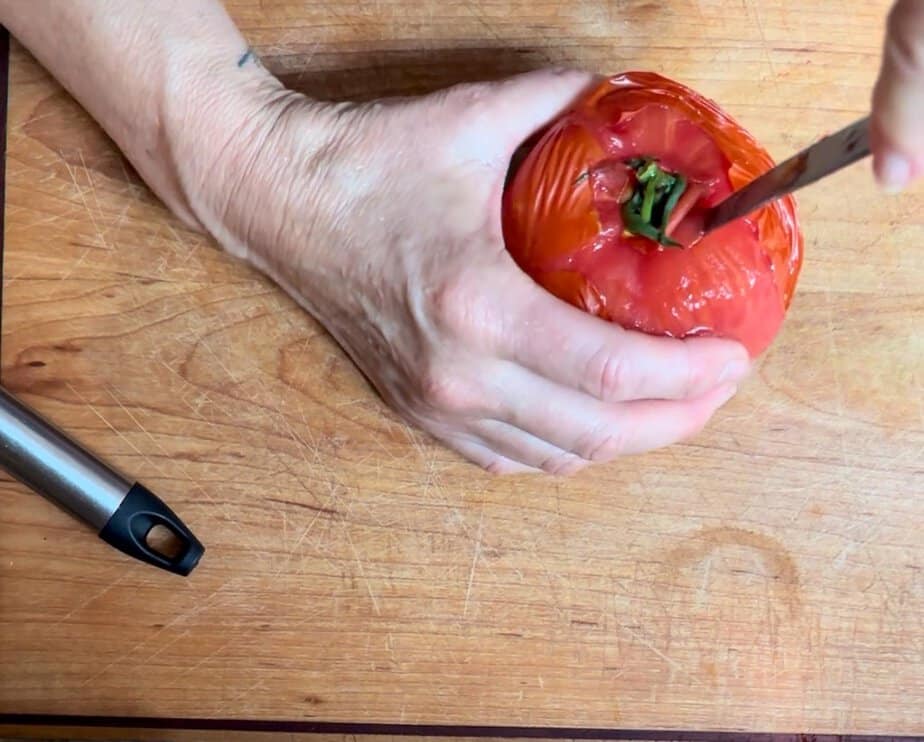 Hand using a pairing knife to core a tomato.