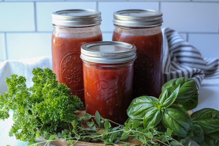Slow cooker spaghetti sauce in three mason jars with fresh herbs surrounding the jars.