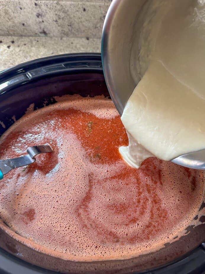 White sauce being added to the pureed soup in the crockpot base.