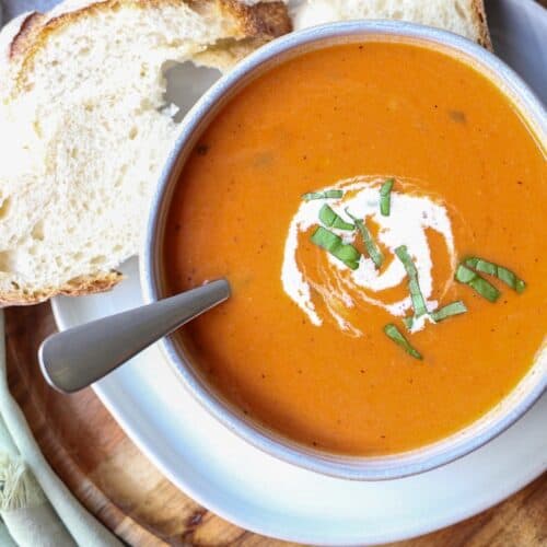 Creamy tomato soup in a bowl with fresh bread on the side.
