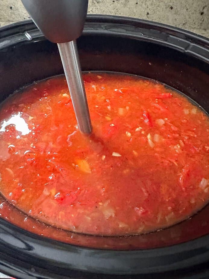 Immersion blender being used to blend the soup in the crockpot base.