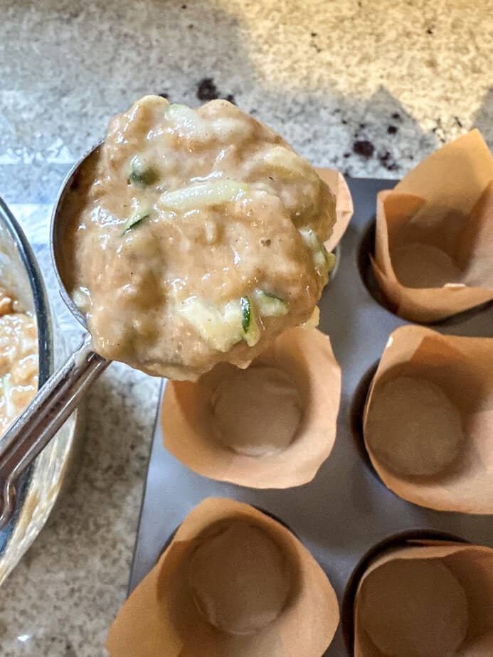 A scoop adding muffin batter to prepared muffin pan.