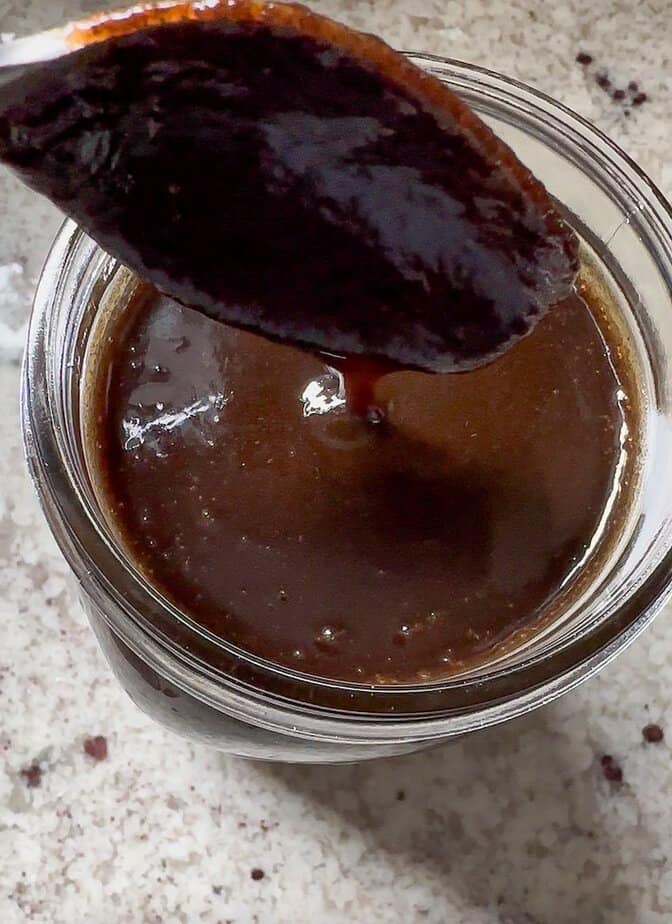 Spoon pouring fresh vanilla bean paste over jar. 